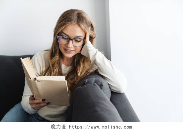 一个戴眼镜的女人坐在沙发上看书年轻快乐女人坐在沙发上看书的照片